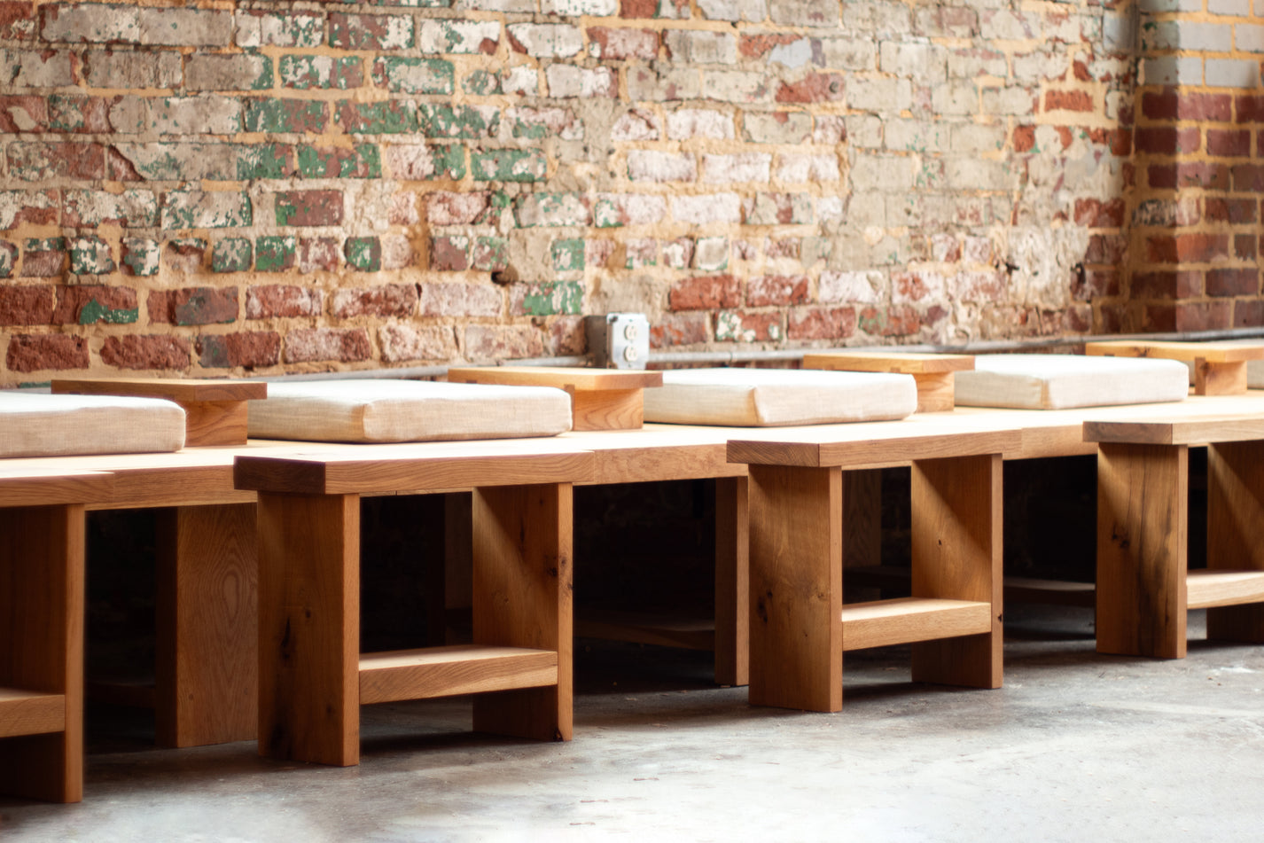 Row of wooden benches against a brick wall.